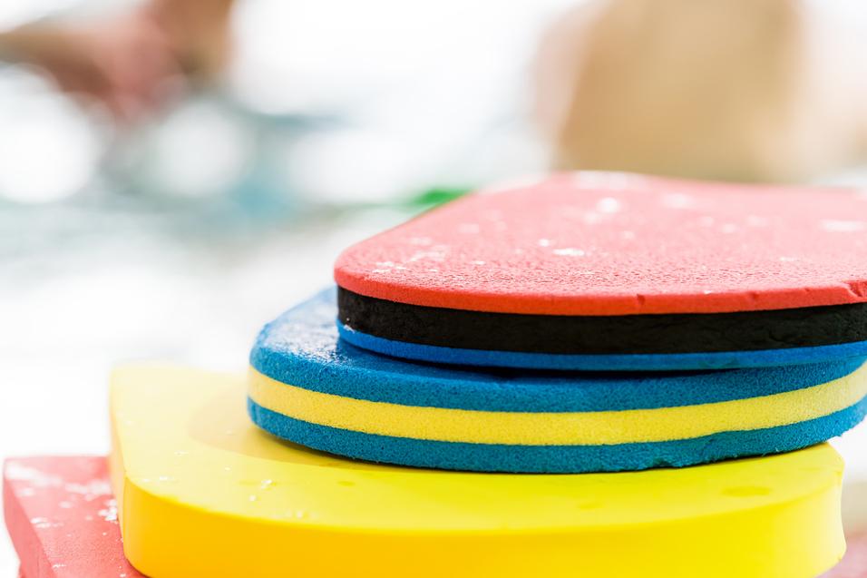Bunte Schwimmbretter in verschiedenen Farben übereinander gestapelt, mit Wassertropfen auf der Oberfläche.